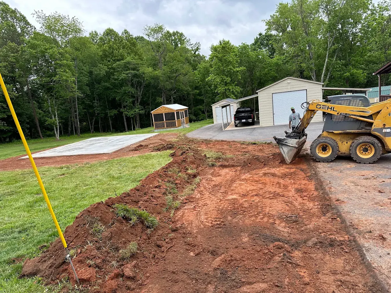 Skid steer grading exposed soil beside a residential driveway and garage
