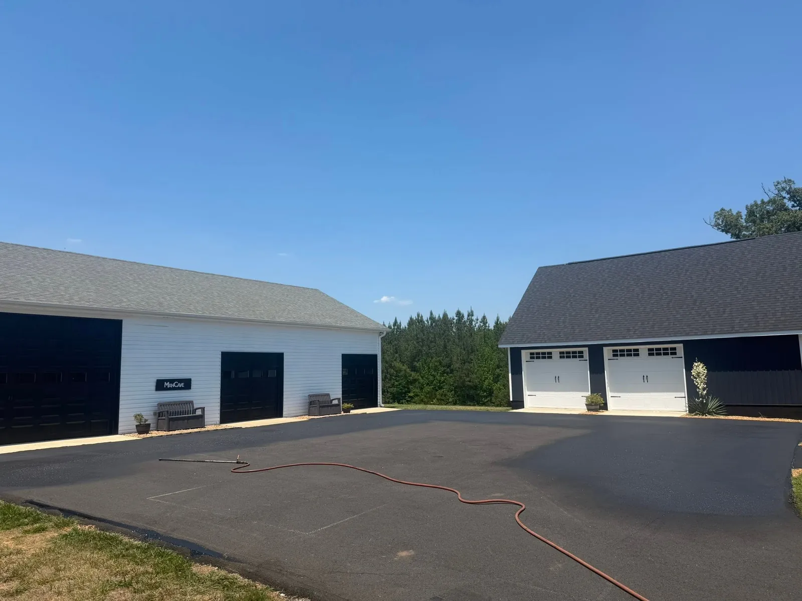 Partially treated asphalt courtyard with a spray hose in front of detached garages