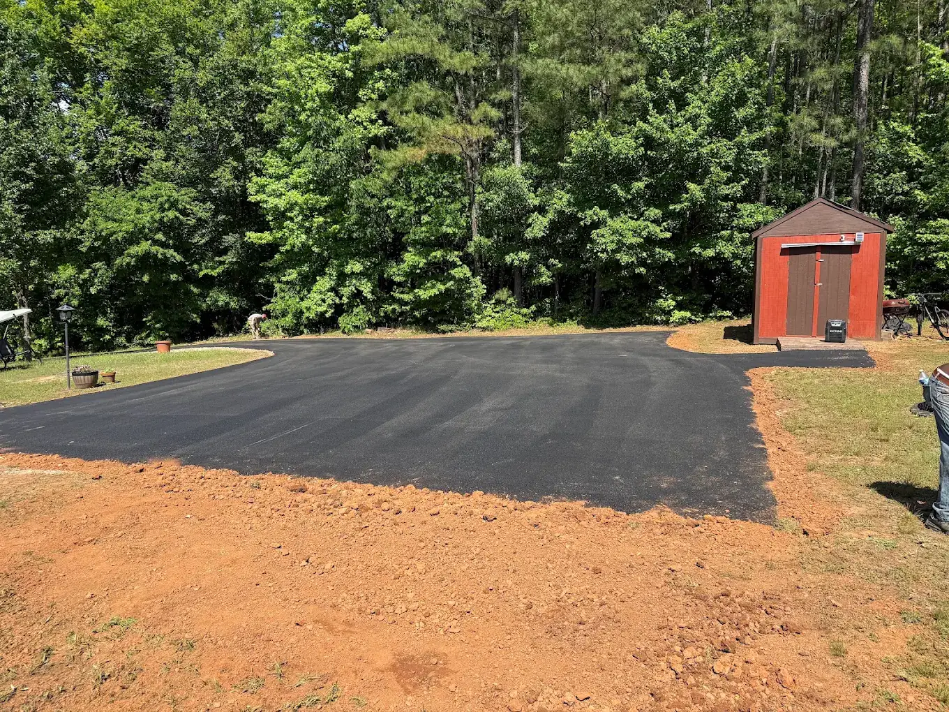 Completed rectangular asphalt pad beside a red shed