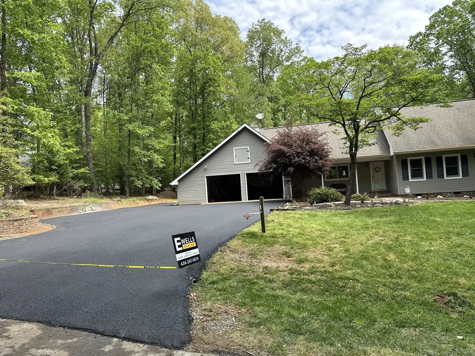 Newly paved driveway leading to a gray home and attached garage