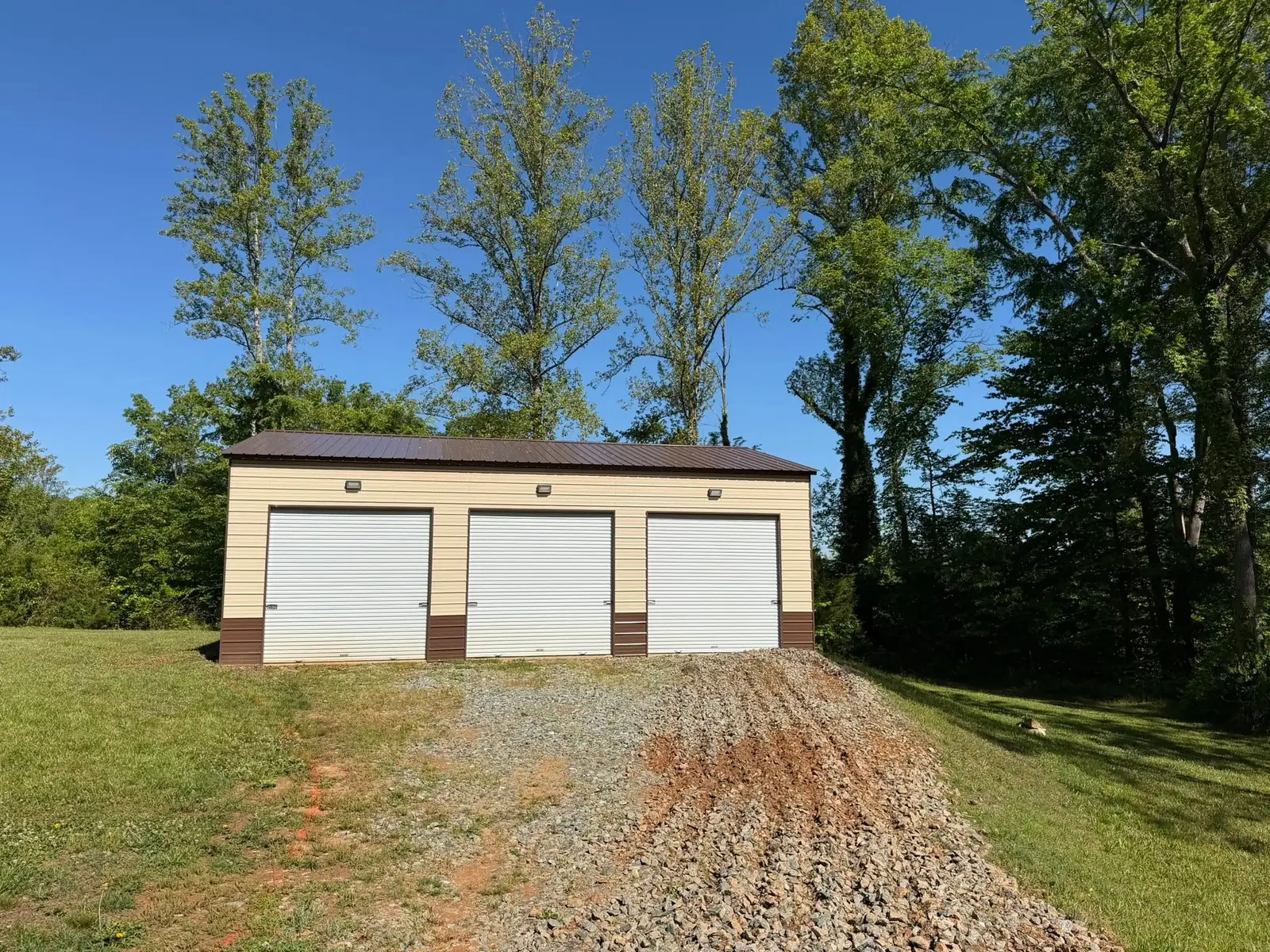 Gravel and bare-earth driveway in front of a detached three-car garage before asphalt paving